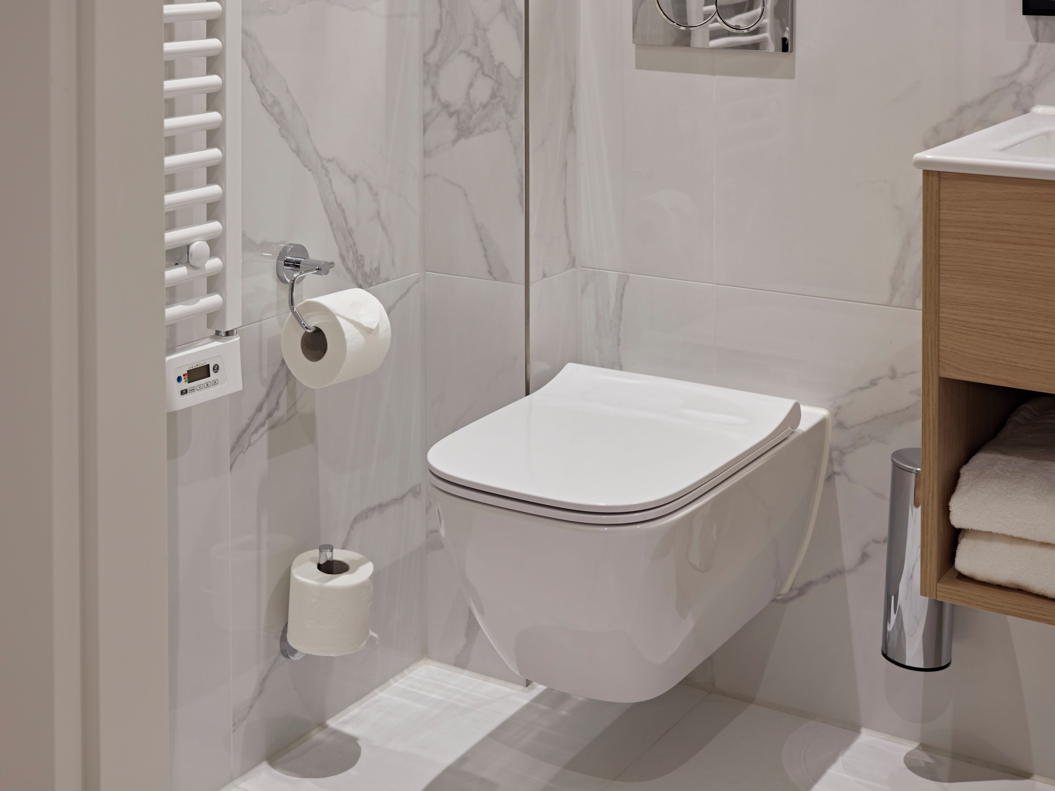 Een moderne badkamer met toilet, marmeren wanden, een handdoekhouder en een toiletrolhouder.