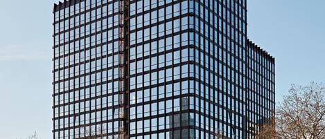 Un immeuble moderne de grande hauteur, avec une façade constituée d’une grille de fenêtres, une ligne de tramway devant et une enseigne indiquant « Fair Play ».