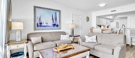 A modern living room with two grey sofas, a wooden coffee table, and a painting of sailboats.