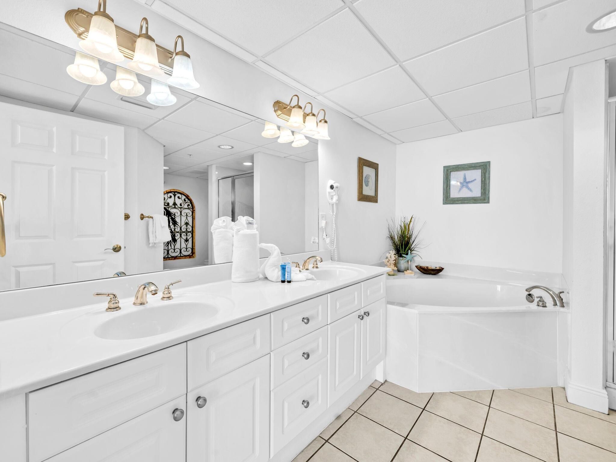 A modern bathroom with a large mirror, two sinks, a bathtub, and a shower. There are towels and toiletries on the counter.