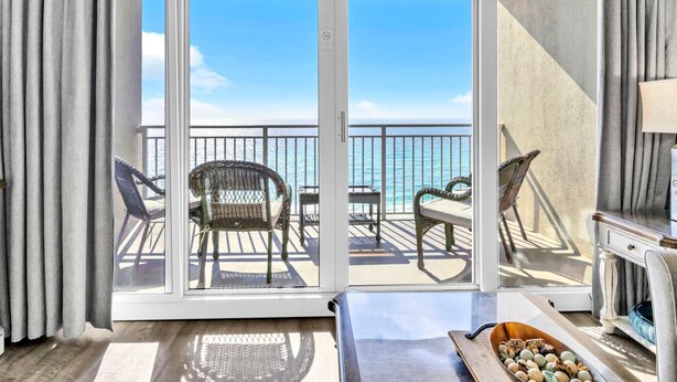 A hotel room with a sliding glass door leading to a balcony with outdoor furniture and a view of the sea. - Emerald Beach 931 (Panama City Beach)