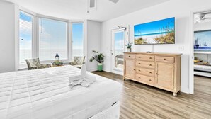 A spacious bedroom with a large bed, a wooden dresser, a ceiling fan, and a beach-themed painting on the wall. - Emerald Beach 931 (Panama City Beach)