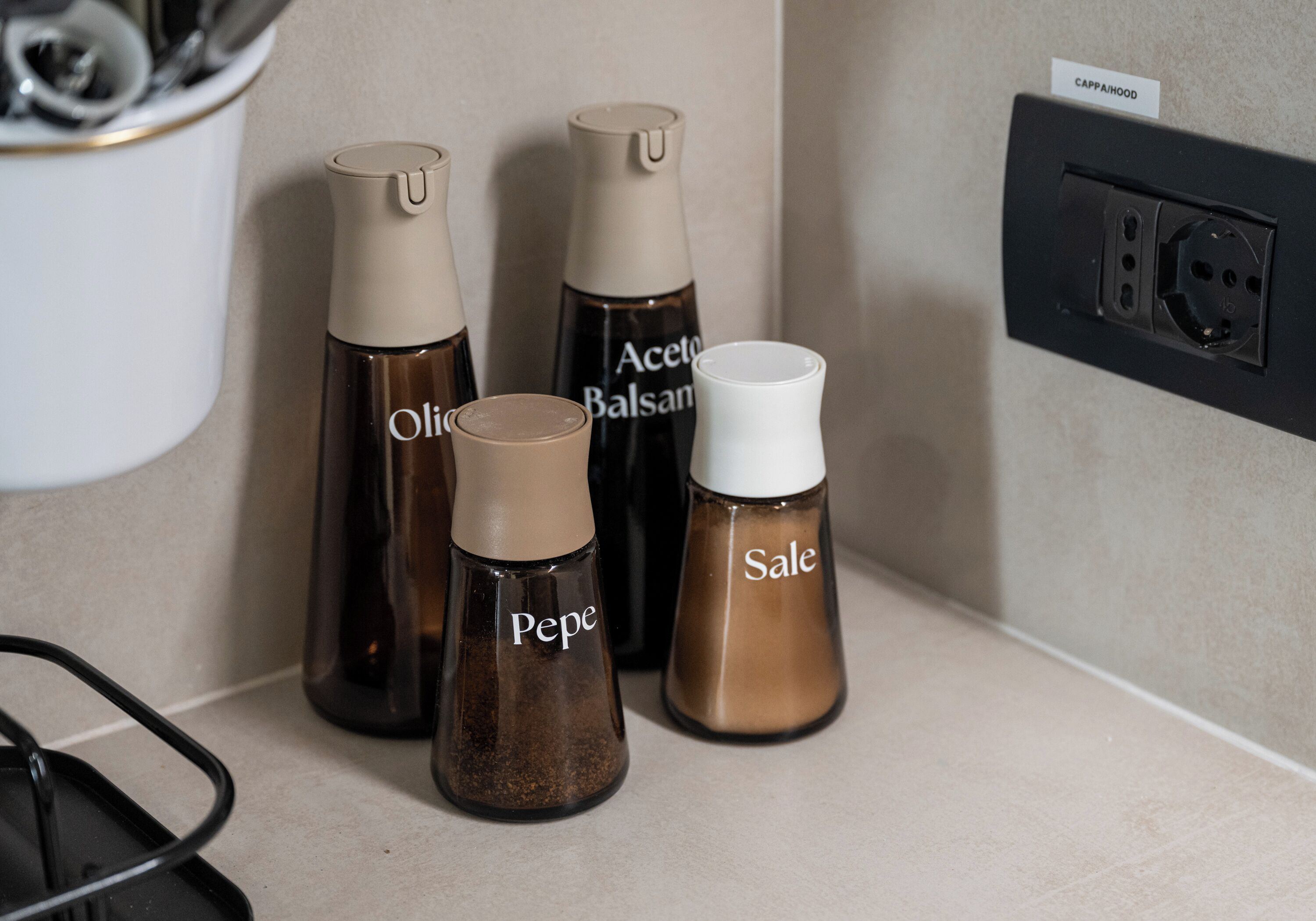 Vier Gewürzflaschen mit den Aufschriften ‚Olio‘, ‚Aceto Balsamico‘, ‚Pepe‘ und ‚Sale‘ auf einer Küchenarbeitsplatte.
