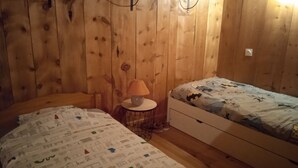 Ein Zimmer mit Holzwänden und zwei Betten, eines mit einem gemusterten Überwurf und das andere mit einem Batman-Motiv.