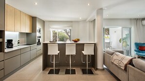 Une cuisine moderne dotée d’un îlot central, de trois tabourets de bar et d’un coin repas comprenant un canapé et une chaise bleue.