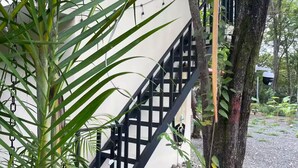 Un escalier avec une rampe en métal noir mène à un bâtiment blanc, qui est entouré de verdure et bordé d’un chemin de gravier.