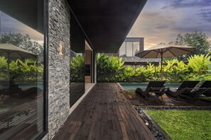 A modern outdoor pool area with wooden decking, lounge chairs, and umbrellas. - Seven Stones Villas (Ubud)