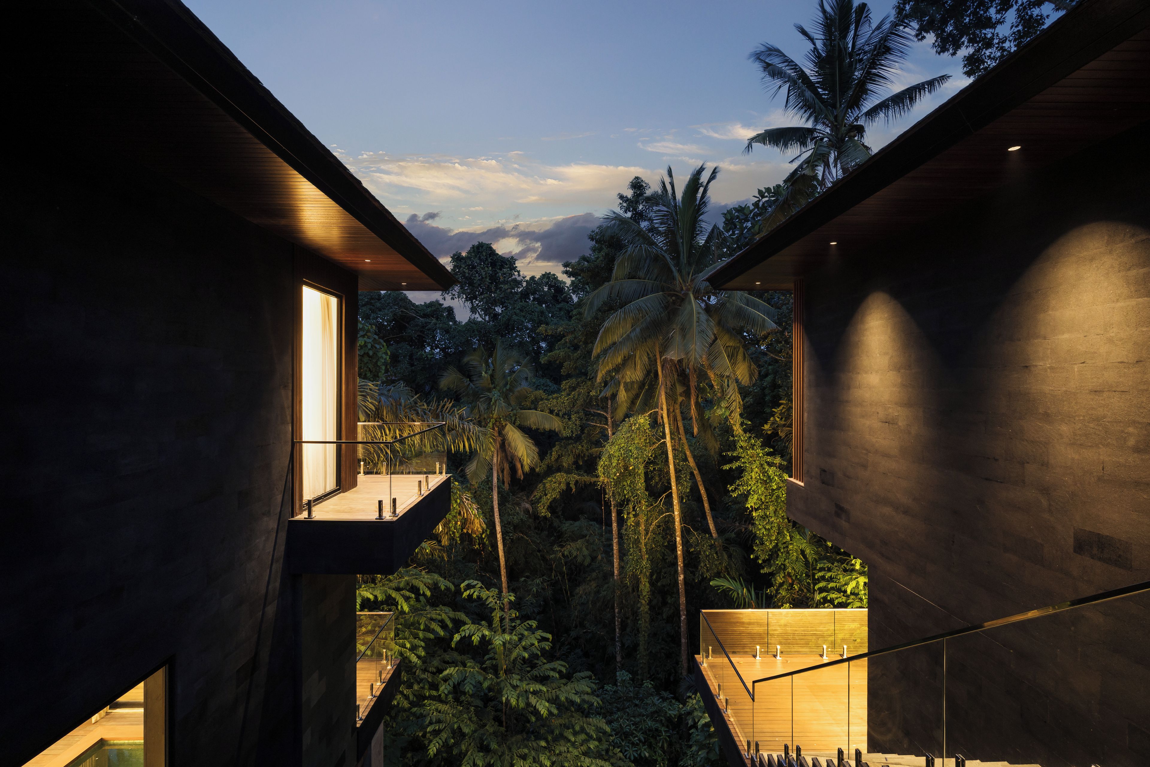A modern building with a glass balcony overlooking a tropical landscape.