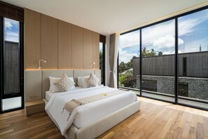 A modern bedroom with a large bed, wooden paneling, and a view of a garden and building through large windows. - Seven Stones Villas (Ubud)