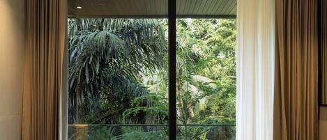 A modern indoor swimming pool with a glass barrier, surrounded by beige curtains and a view of lush greenery.