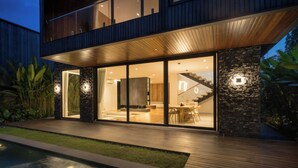 A modern two-story house with large glass windows, a wooden deck, and a swimming pool. - Seven Stones Villas (Ubud)