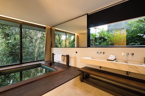 A modern bathroom with a wooden bench, a large mirror, and a view of lush greenery outside. - Seven Stones Villas (Ubud)