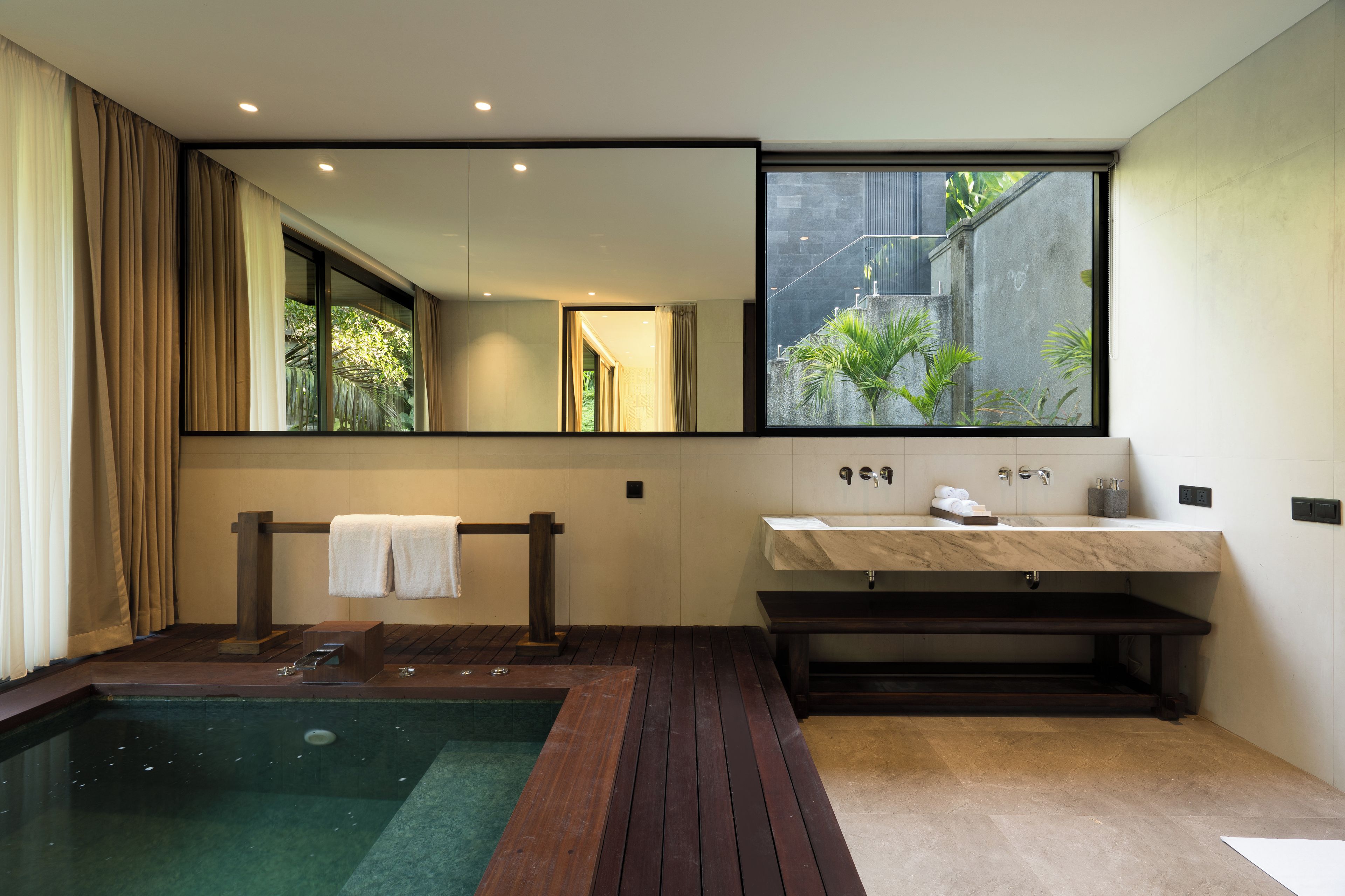 Un bagno moderno con un'ampia finestra, una panca in legno, una vasca da bagno e un lavandino con piano in marmo.