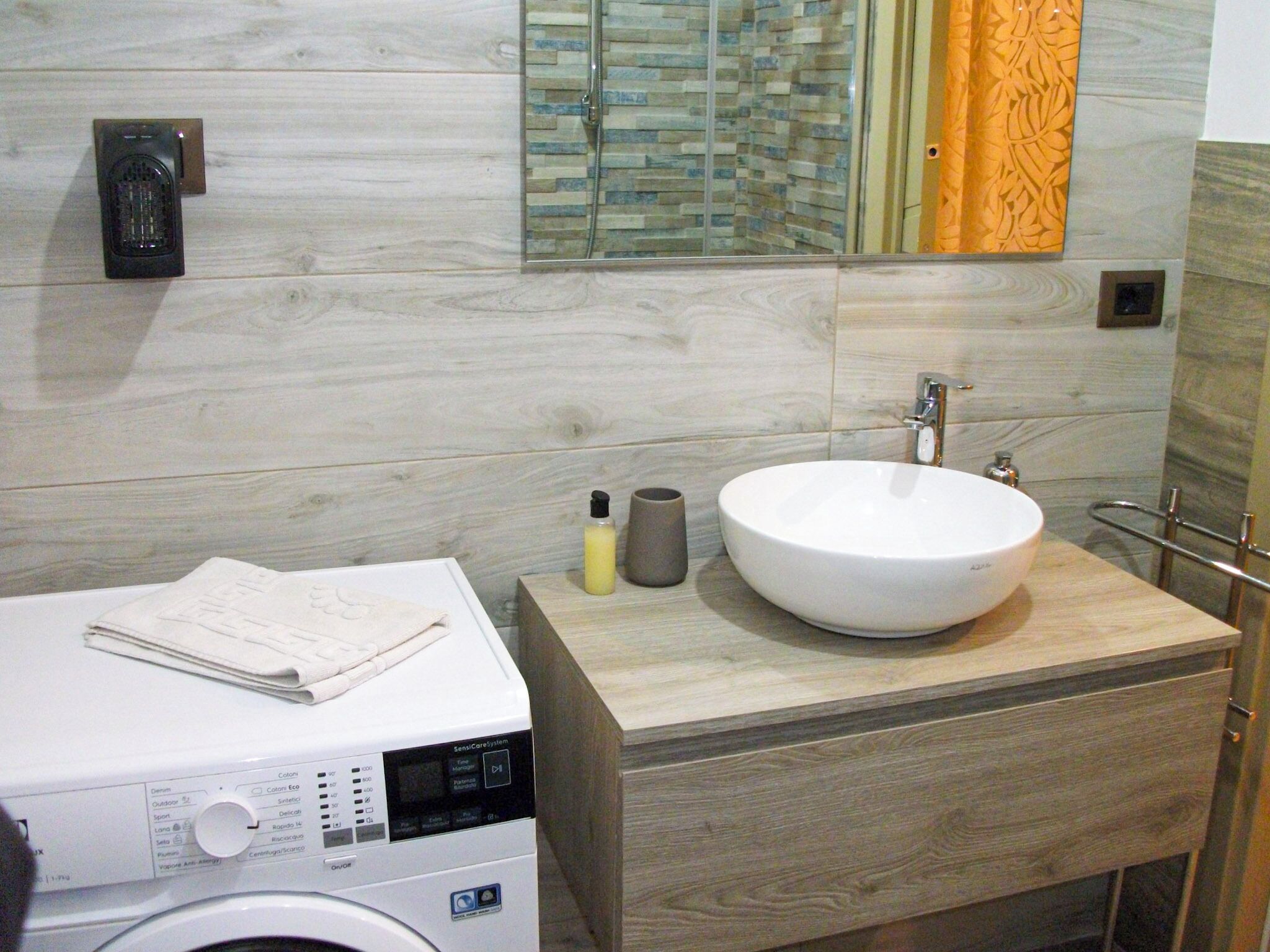 A modern bathroom with a large sink, a washing machine, and a mirror with a decorative backsplash.