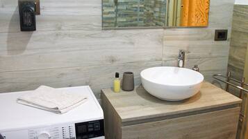 A modern bathroom with a large sink, a washing machine, and a mirror with a decorative backsplash.