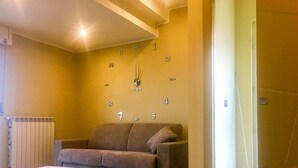 A living room with a beige sofa, a white ottoman, and a wall clock. - Belvedere Vallata Affitti Brevi (Vallata)