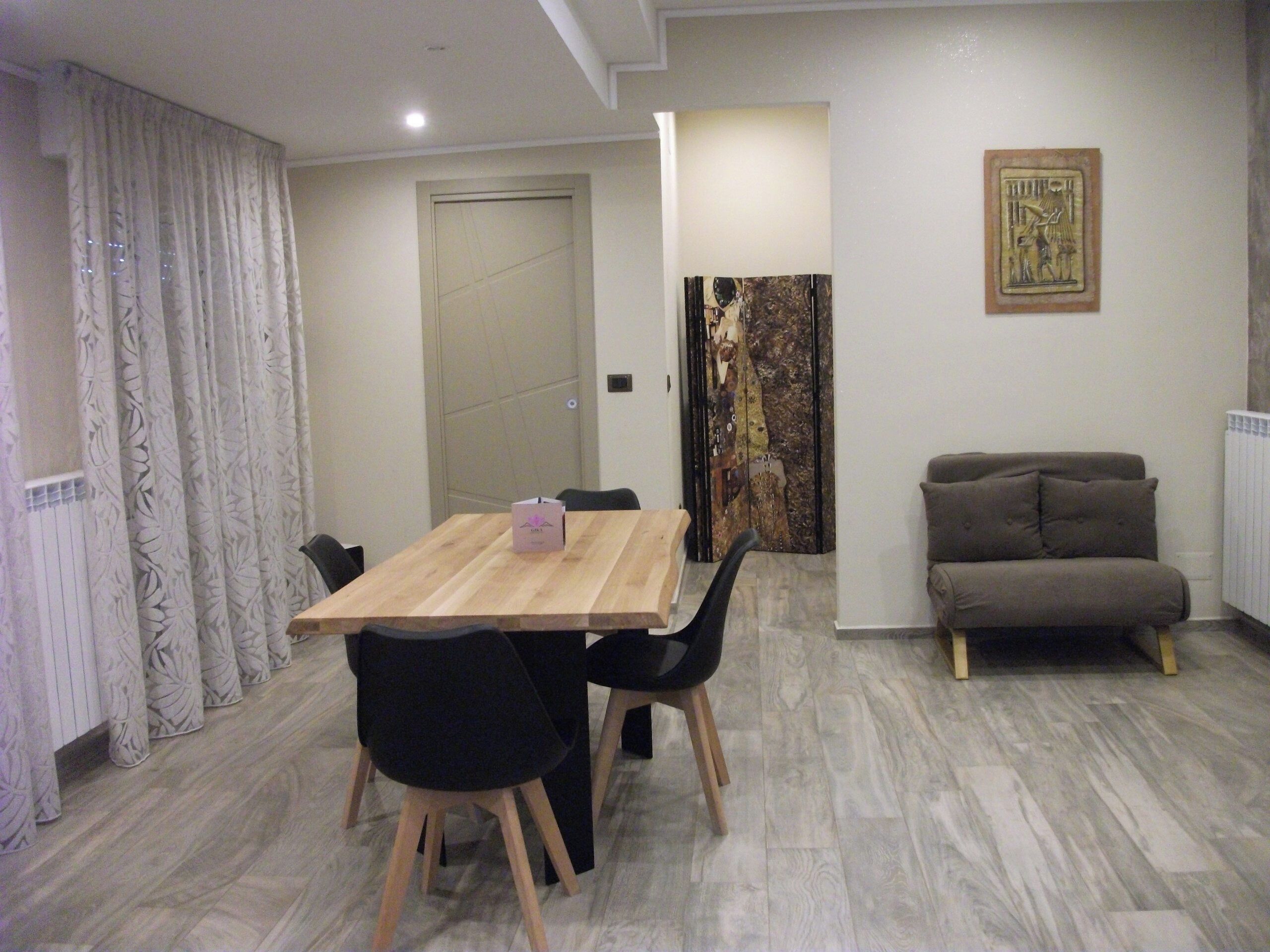 A dining area with a wooden table and chairs, a sofa, and a radiator.