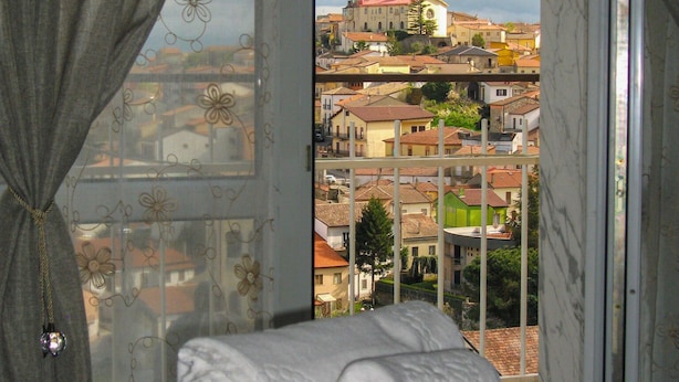 A bed with a view of a cityscape through a window with curtains. - Belvedere Vallata Affitti Brevi (Vallata)