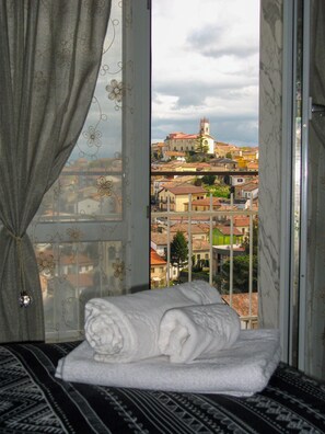 Una cama con vista a un paisaje urbano a través de una ventana con cortinas.