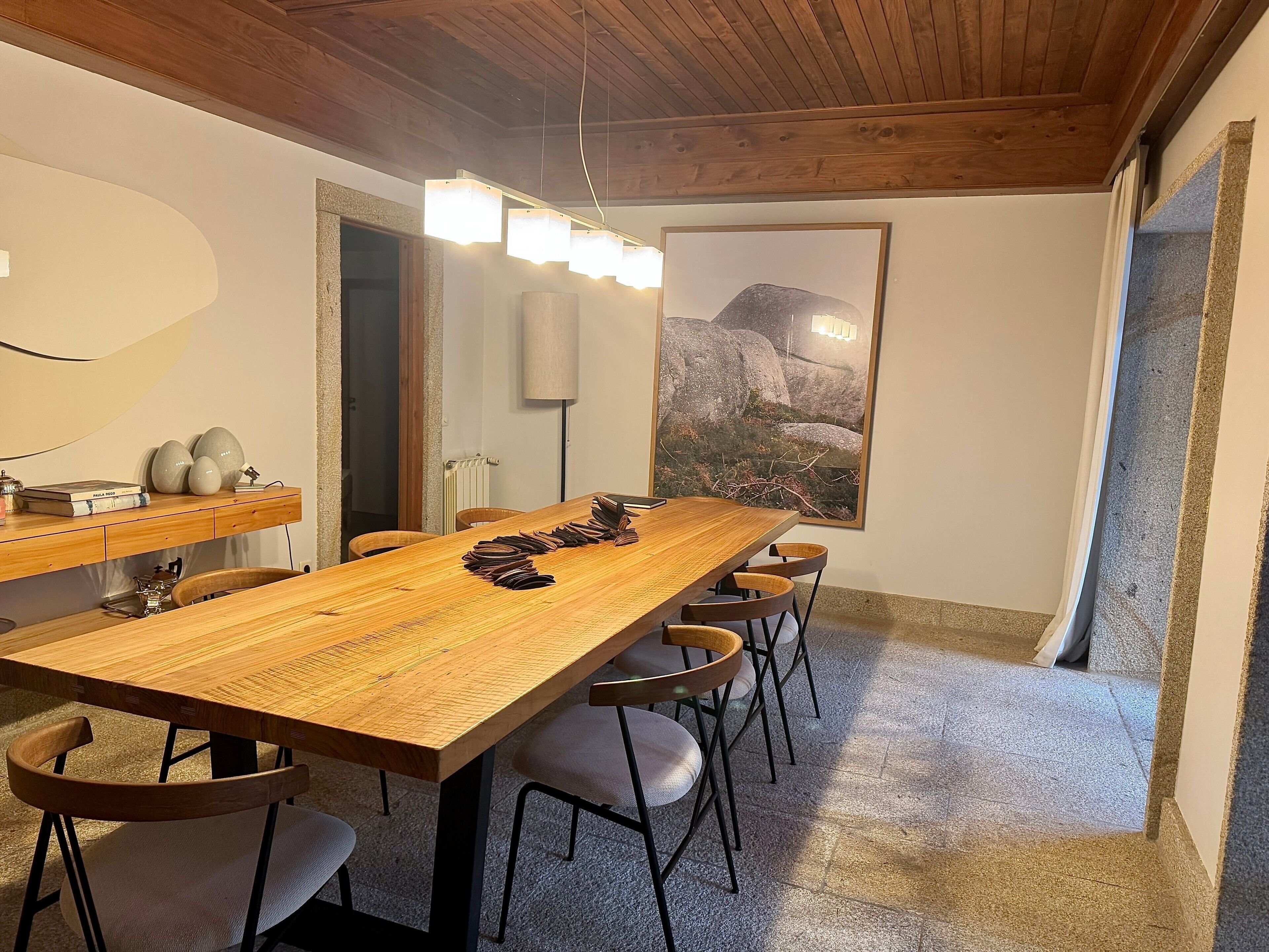 Un comedor con una mesa de madera, sillas, una lámpara y un cuadro en la pared.