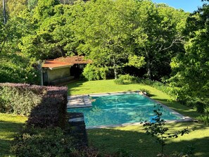 Una piscina circondata da vegetazione rigogliosa e un piccolo edificio con tetto rosso.
