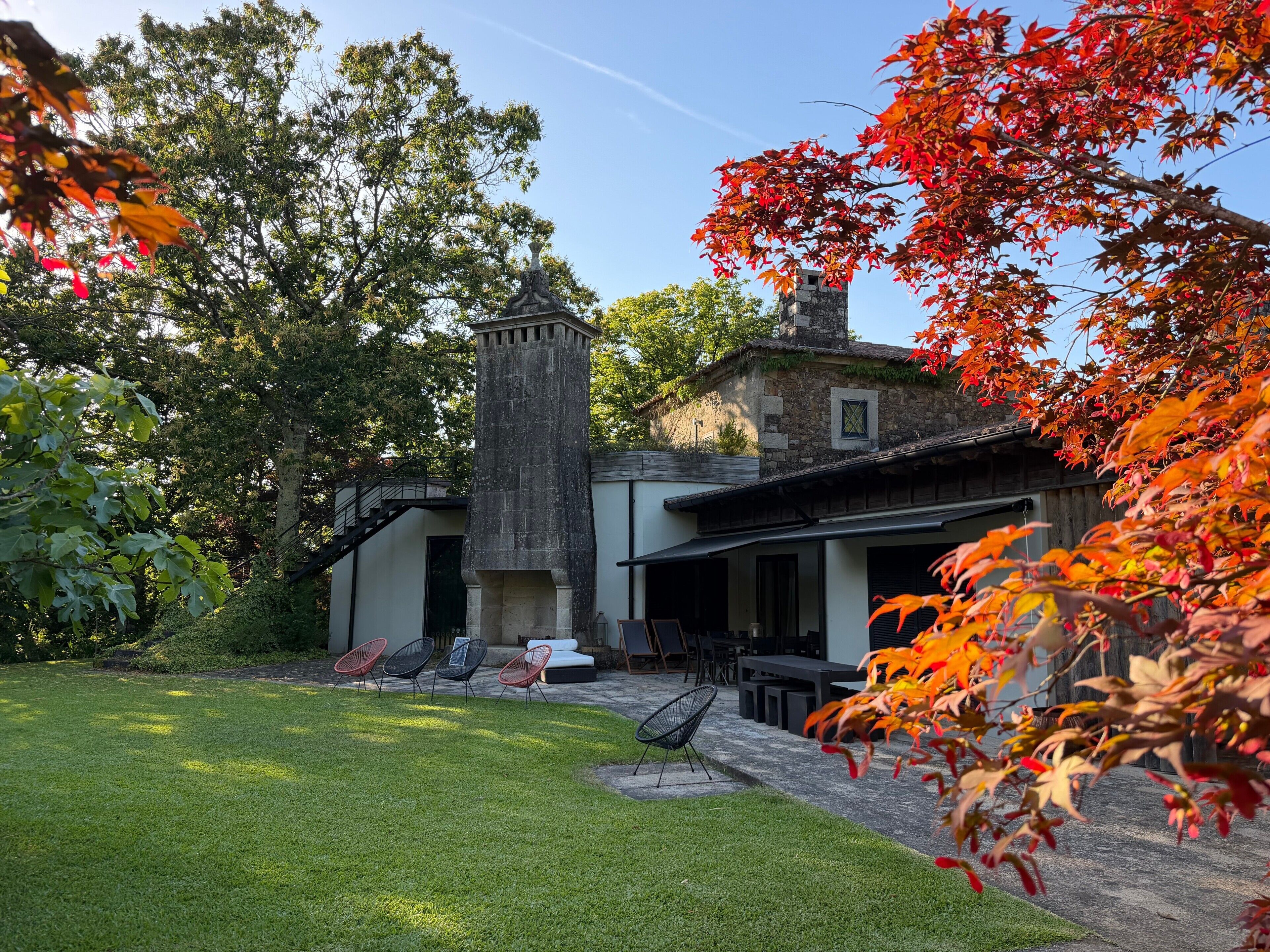 Un bâtiment doté d’une tour en pierre, d’un patio avec des sièges en plein air et d’une pelouse bien entretenue.