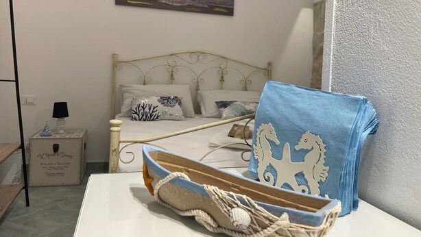 A bedroom with a bed, a nightstand, a lamp, and a decorative item on the table. - LUISA ROOM (Sampieri)