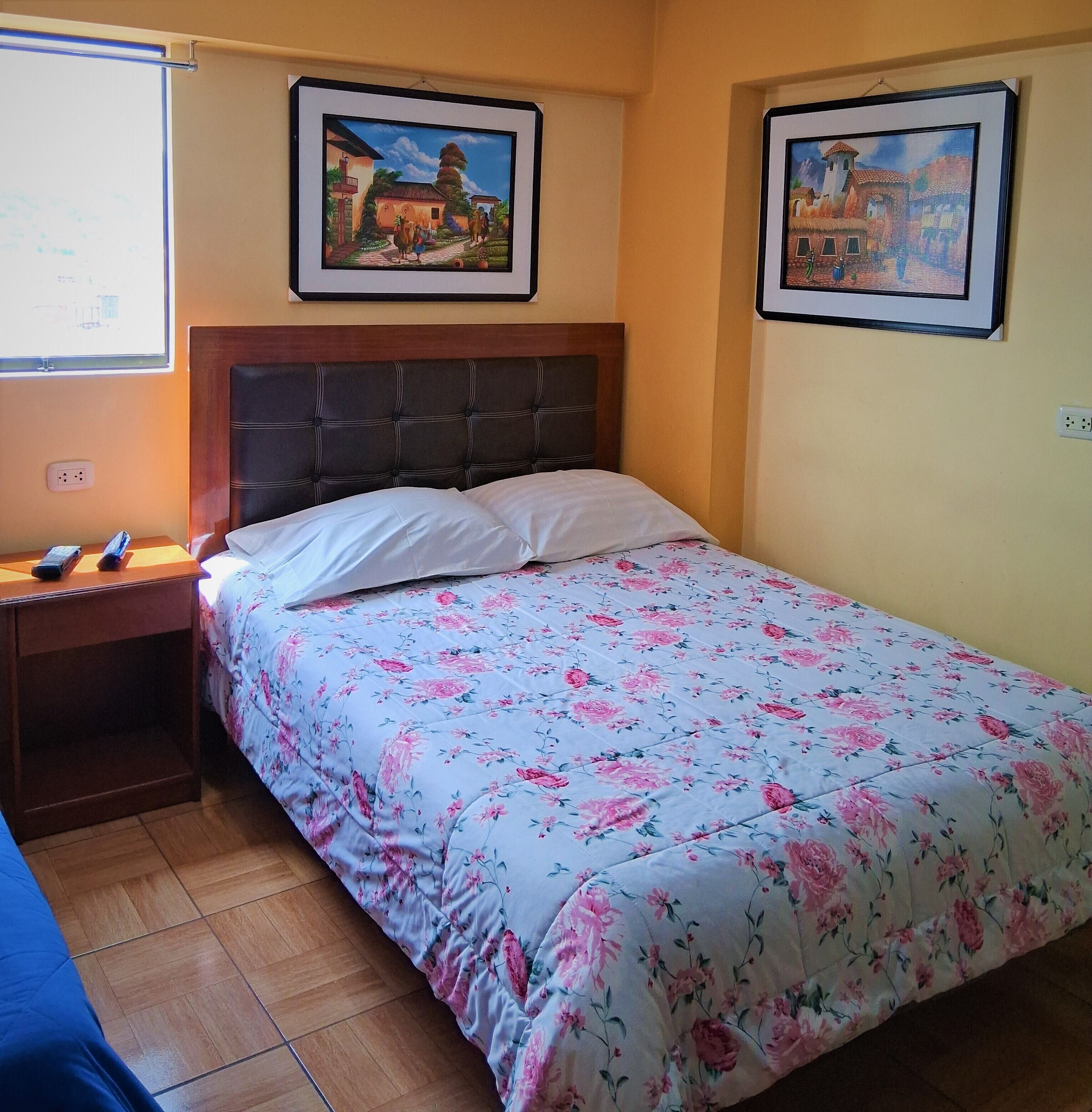 A bedroom with a bed, a nightstand, a wall-mounted TV, and two framed pictures.