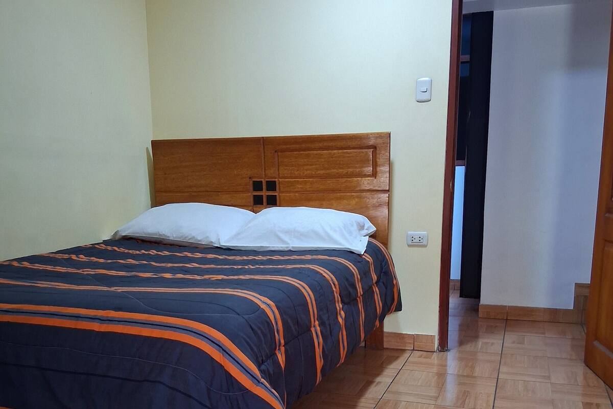 Ein Einzelbett mit Holz-Kopfteil in einem Zimmer mit gefliestem Boden.
