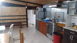 A compact kitchen with a stove, oven, and refrigerator. There is a dining table with chairs and a red trash bin. - hostal kuntur cusco (Cusco)