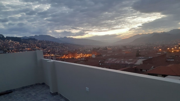 A rooftop terrace with a view of a cityscape at dusk, featuring distant mountains and a cloudy sky. - hostal kuntur cusco (Cusco)