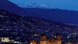 A historic town with a prominent church featuring a bell tower, surrounded by a densely populated area with visible residential buildings and a mountain range in the background. - hostal kuntur cusco (Cusco)