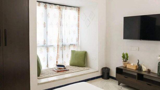 Ein Schlafzimmer mit Fensterbank, einem Bett, einem Fernseher, einer kleinen Pflanze und einem Mülleimer.