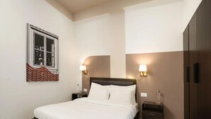 A hotel room with a bed, bedside tables, wall-mounted lamps, a window with a view, and a wardrobe. - Bedchambers Suite Near Sector 29 (Gurugram)