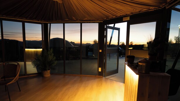 A spacious room with a large sliding glass door leading to an outdoor area, a wooden floor, a chair, and a small table with a plant. - El Refugio del Indio (Archidona)