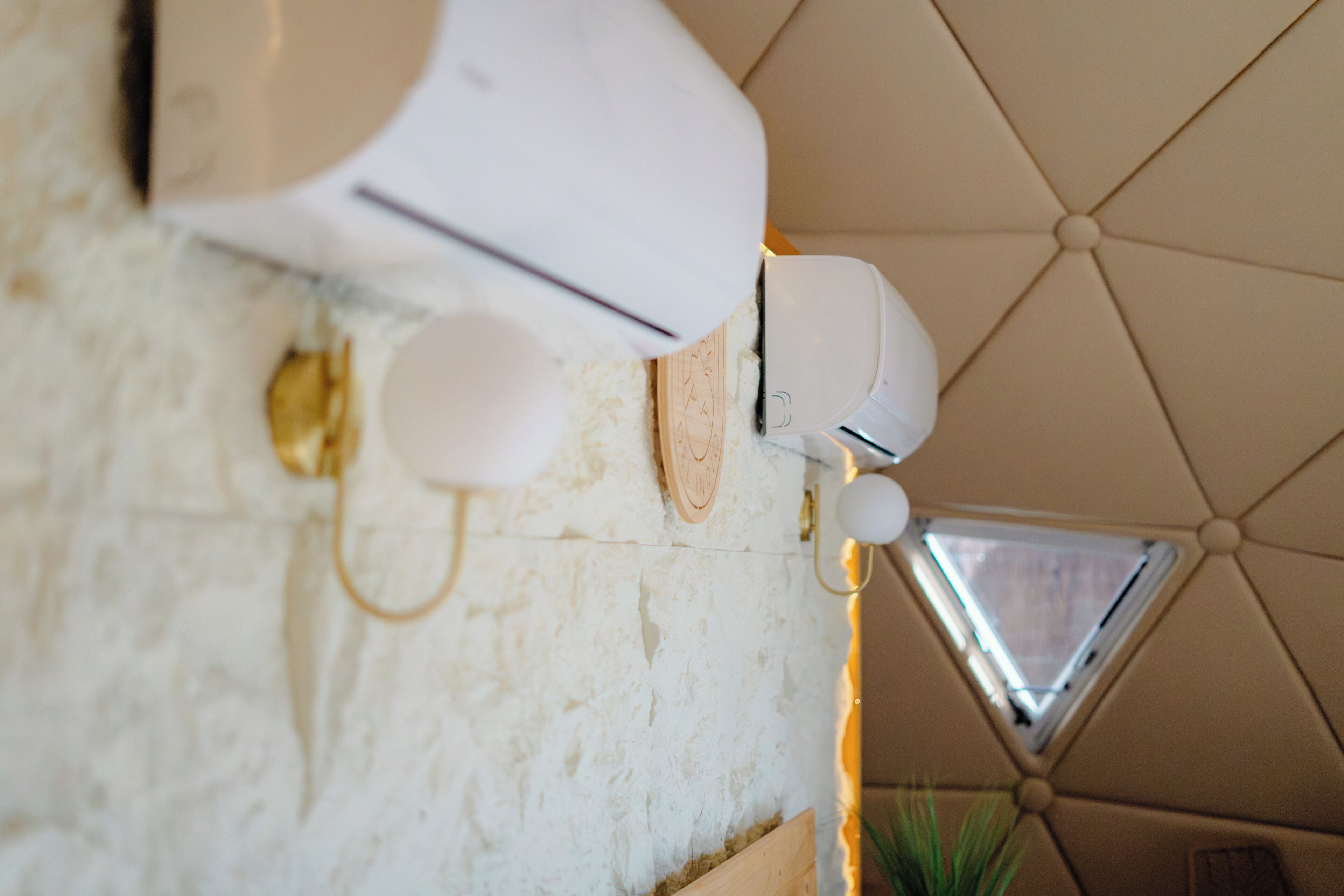A wall-mounted air conditioning unit, a small wooden shelf, and a triangular window.