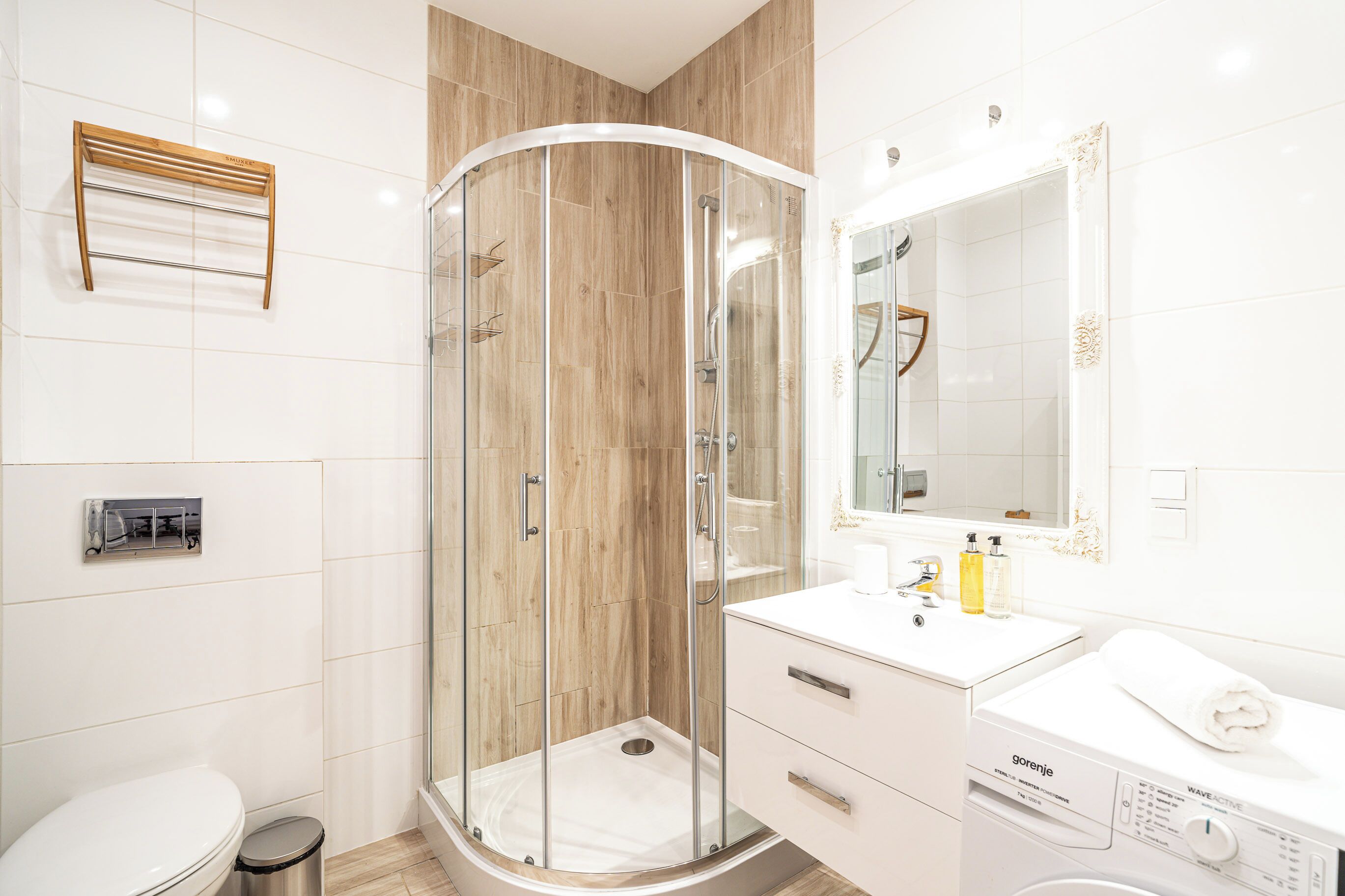 A modern bathroom with a glass-enclosed shower, a white sink with a mirror, and a built-in washing machine.