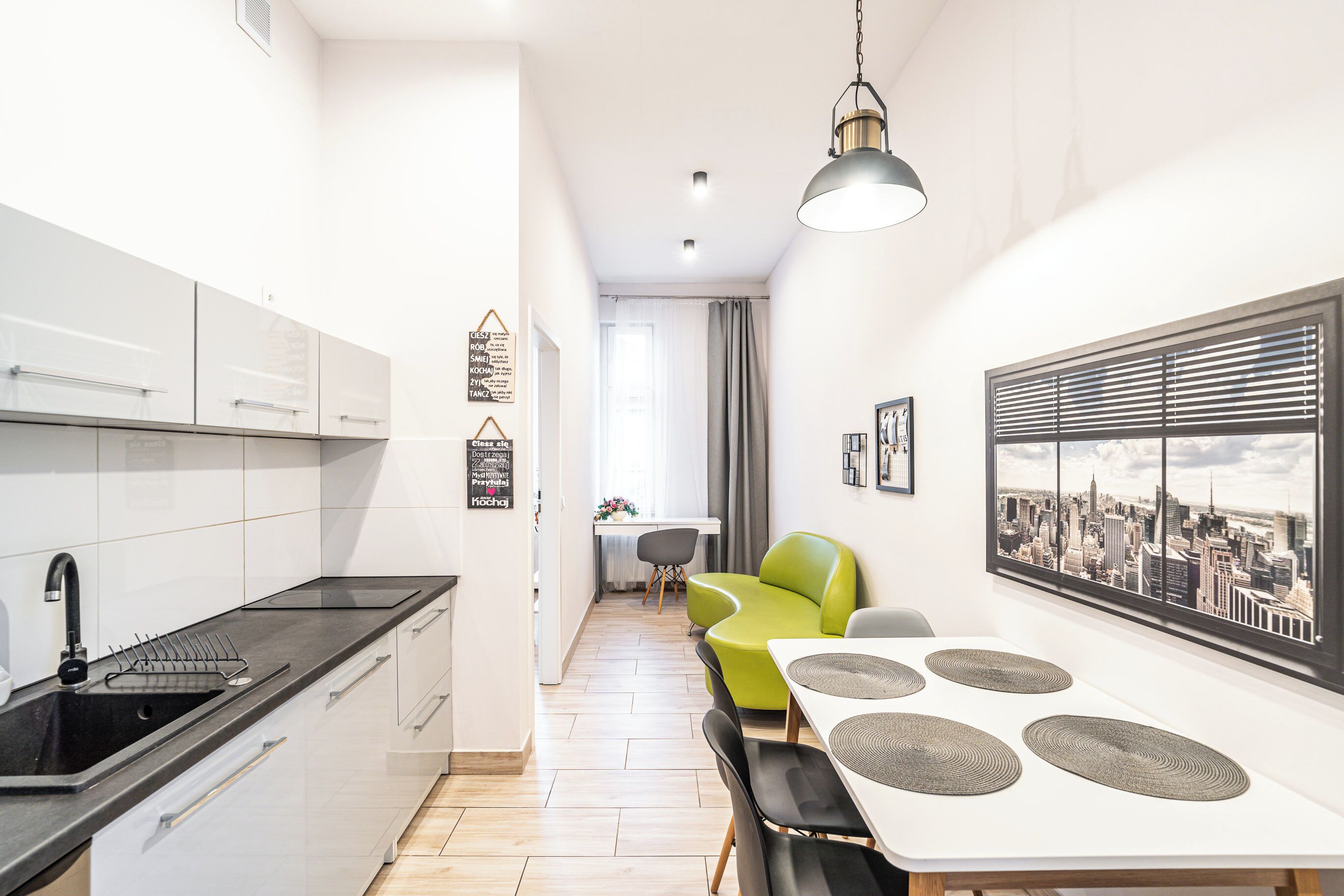 A modern kitchen with white cabinets, a black countertop, and a dining area with a white table and green chairs.