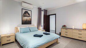 A modern bedroom with a bed, bedside tables, a dresser, and a wall-mounted air conditioner. - Sliema Seaside Penthouse with Terrace (Sliema)
