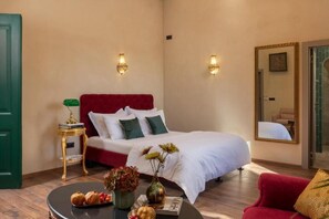 A hotel room with a red upholstered bed, two wall-mounted light fixtures, a round coffee table with decorative items, and a mirror on the wall. - Pervicacia Lux Studios (Dubrovnik)
