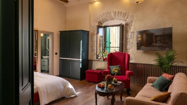 A cozy room with a bed, a red armchair, a sofa, and a dining table with fruit and a vase. - Pervicacia Lux Studios (Dubrovnik)