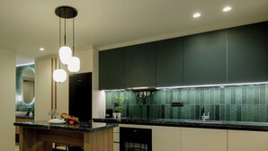 A modern kitchen with dark green cabinets, a marble countertop, and a central island with stools. - Mavili Urban Elegance (Heraklion)