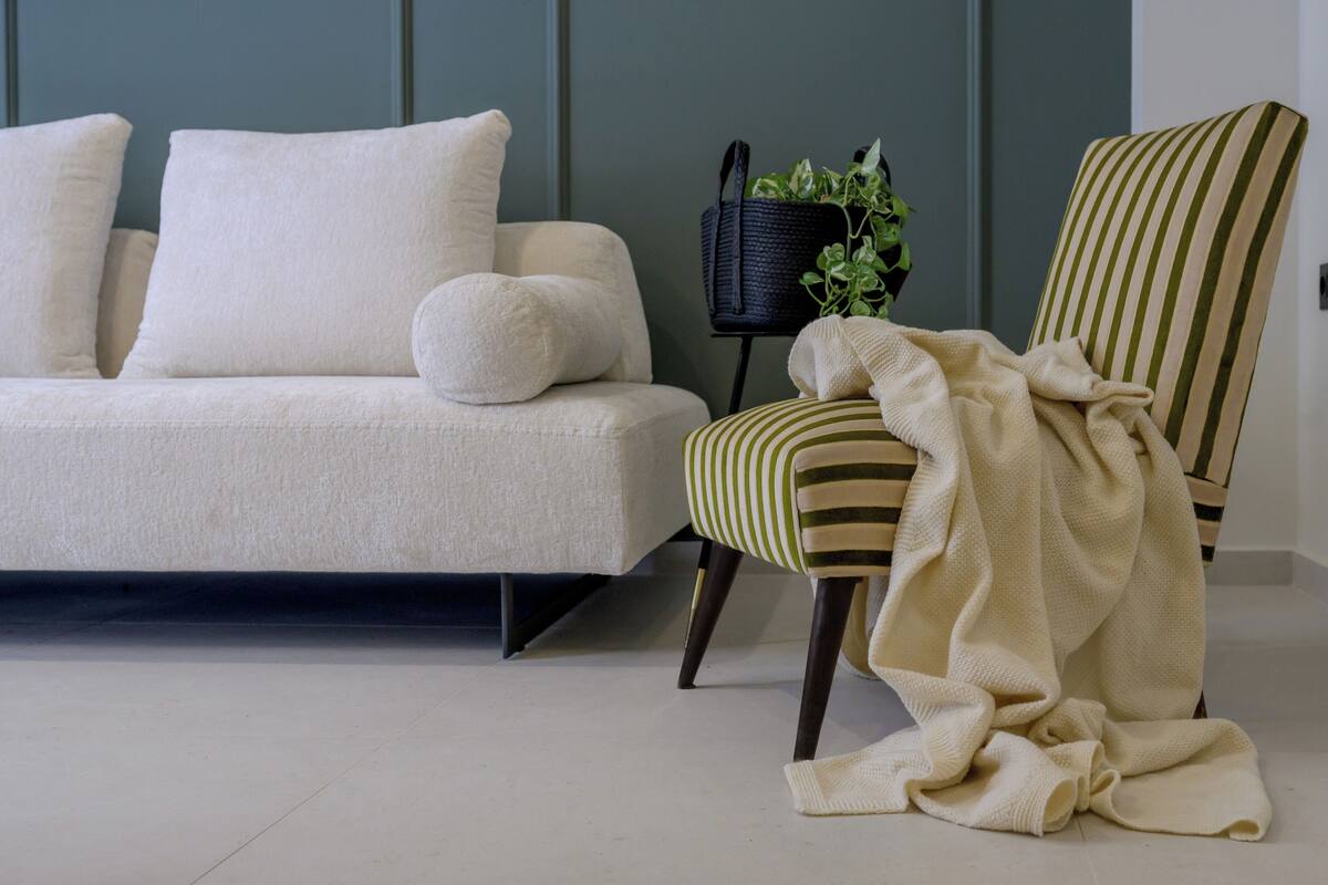 A living room with a sofa, a striped armchair, a small black side table with a plant, and a white blanket on the armchair.