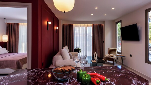 A modern hotel room with a marble dining table, a sofa, a TV, and a view of the outside. - Mavili Urban Elegance (Heraklion)