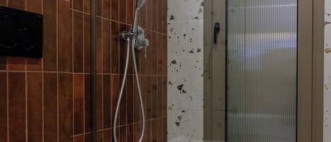 Un baño con inodoro blanco, ducha con puerta de cristal y suelo de baldosas con diversos diseños.