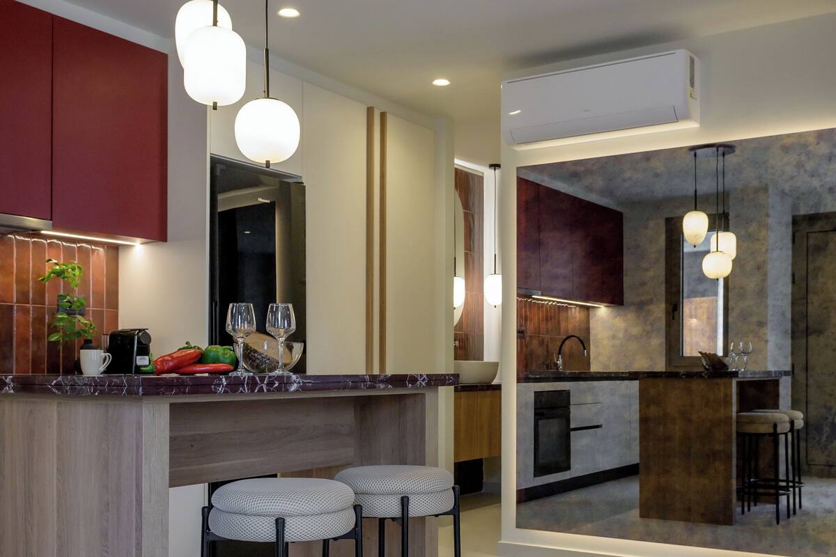 A modern kitchen with a marble countertop, two bar stools, and pendant lighting.