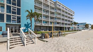 Ein Hotel direkt am Strand mit mehreren Balkonen, Außenmöbeln und einer Treppe zum Eingang.