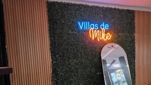 A room with a textured wall, a neon sign reading 'Villas de Mike,' a reflective mirror, and a chair. - Villas de Mike (La Libertad)