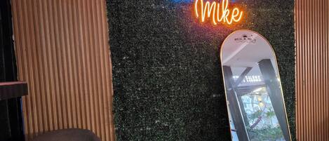 Ett rum med en vägg som har en intressant yta, en neonreklamskylt med texten ”Villas de Mike”, en spegel som reflekterar ljuset och en stol.