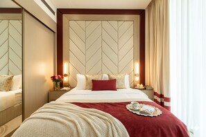 Une chambre d’hôtel avec un grand lit, un miroir, une table de chevet ornée d’un vase de fleurs et un plaid rouge.